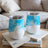 Two white tumblers with blue watercolor designs sit on books.