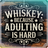 "Whiskey Because Adulting Is Hard" text on a rustic wooden background.