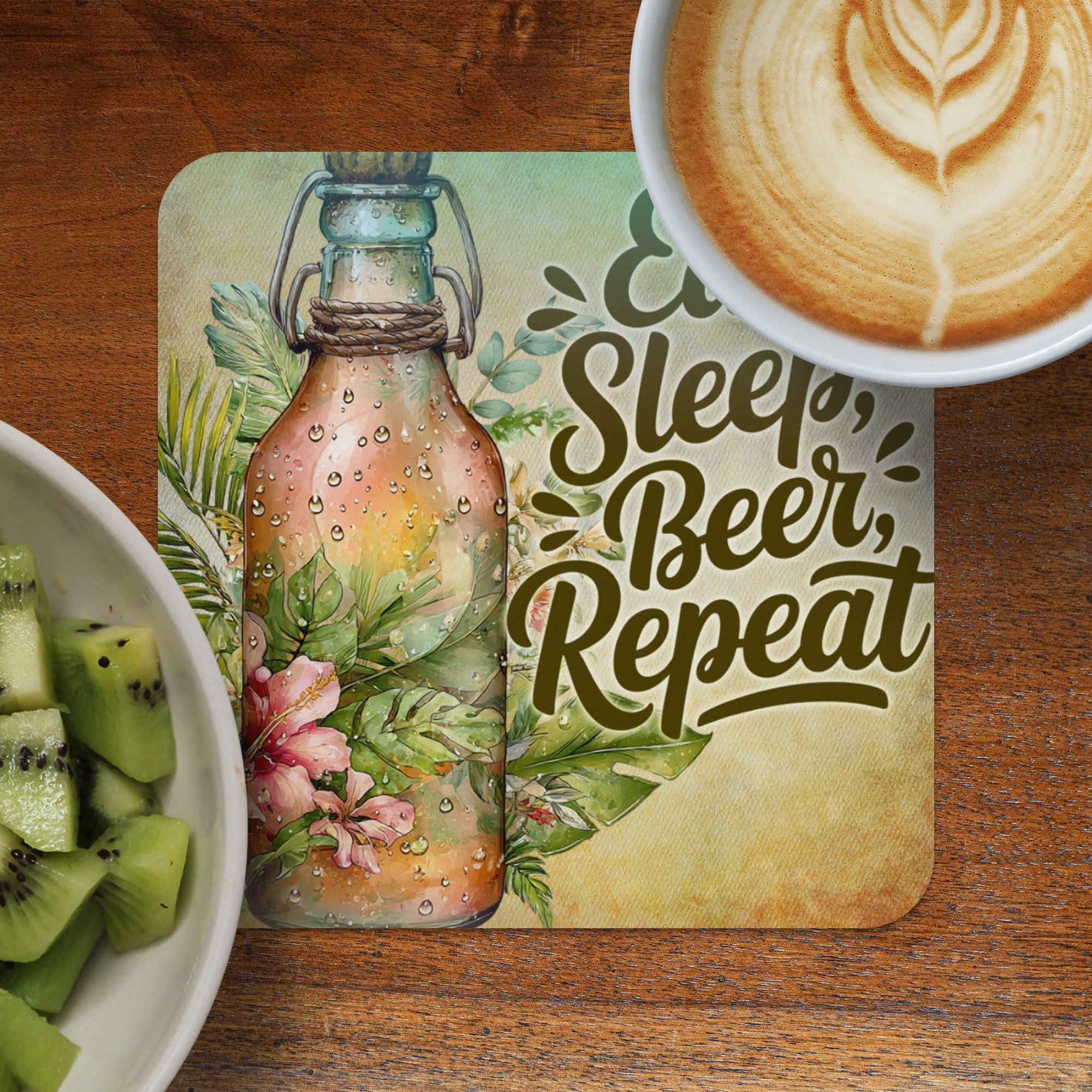 Coaster with "Sleep, Beer, Repeat" text and floral design next to kiwi and coffee.