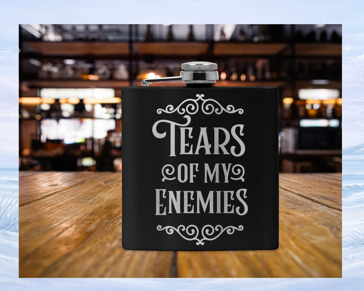 Black flask with "Tears of My Enemies" text on a wooden surface.