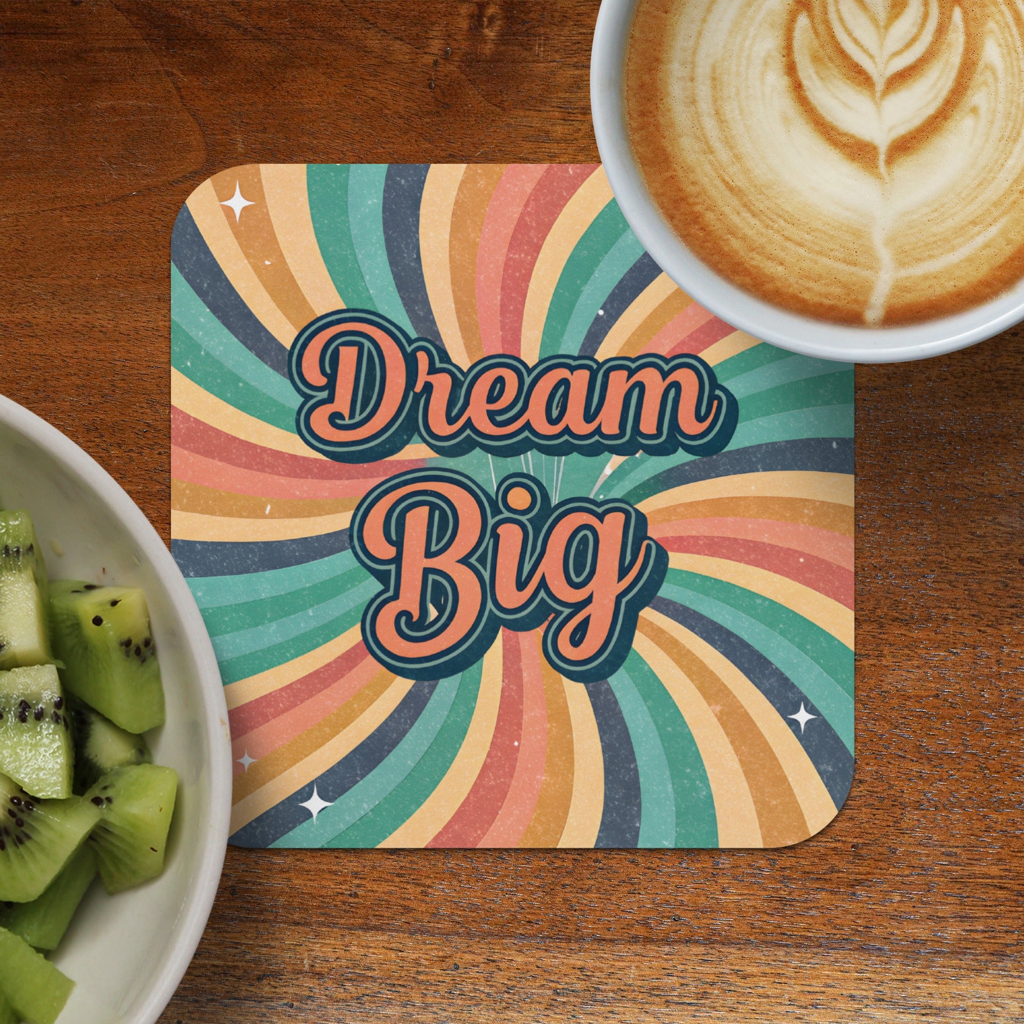 "Dream Big" text on a retro coaster next to kiwi slices and coffee.