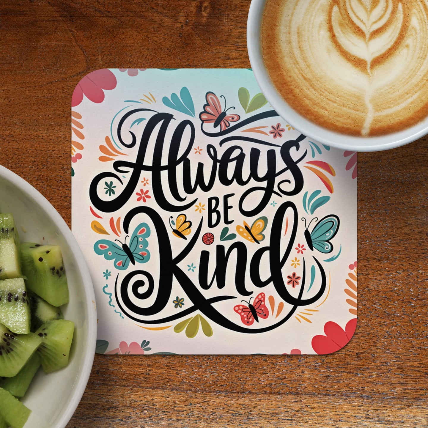 Always be kind sentiment on coaster with coffee and kiwi fruit.