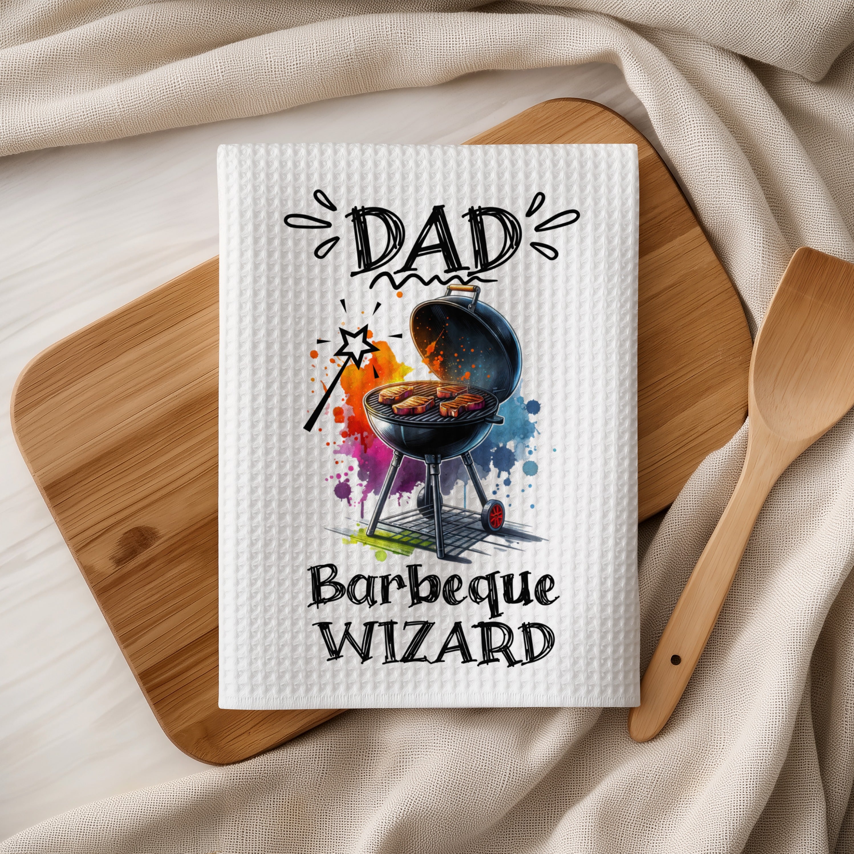 White waffle weave tea towel with "Dad Barbeque Wizard" text and colorful grill graphic.
