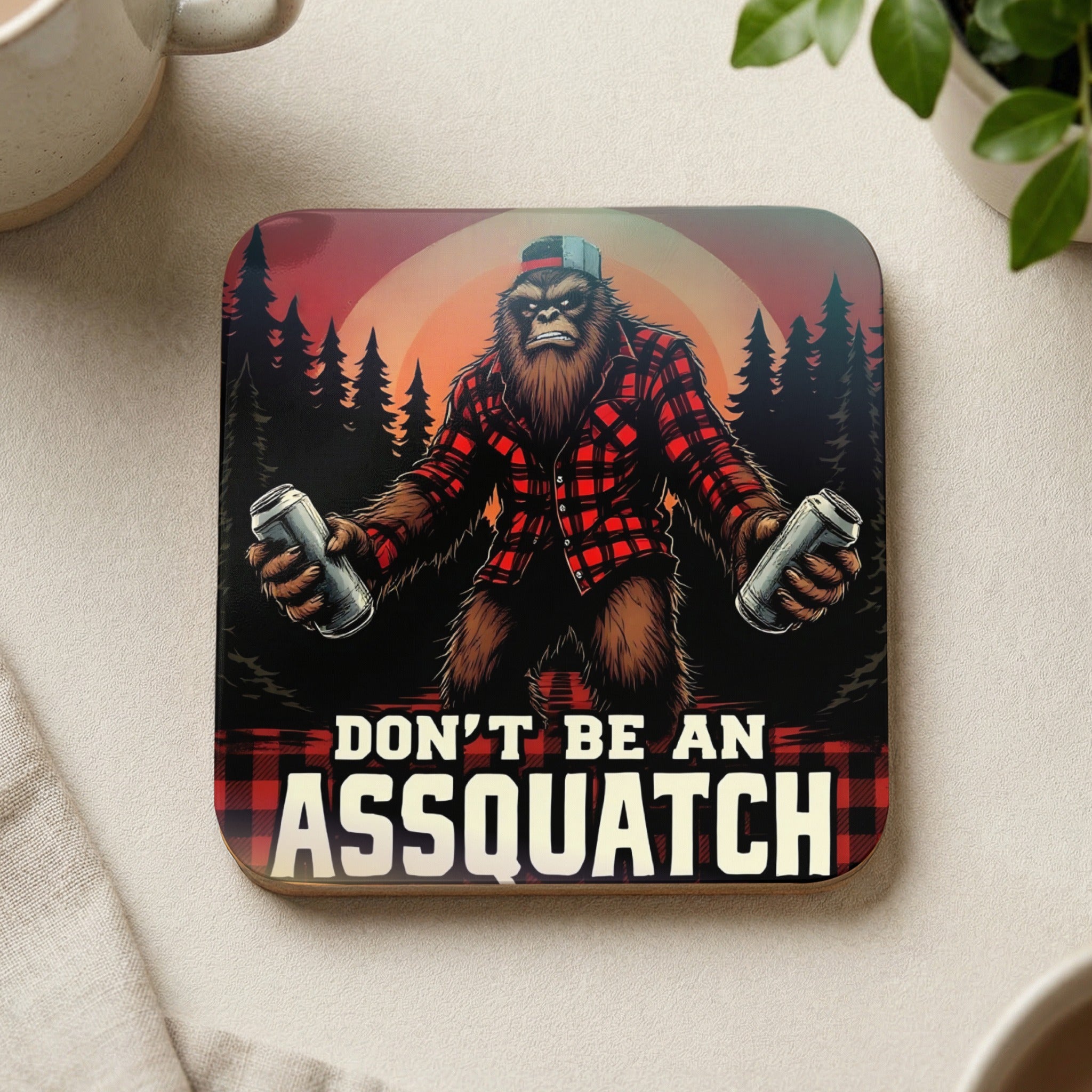 Bigfoot in plaid shirt holds cans, "Don't Be An Assquatch" text.