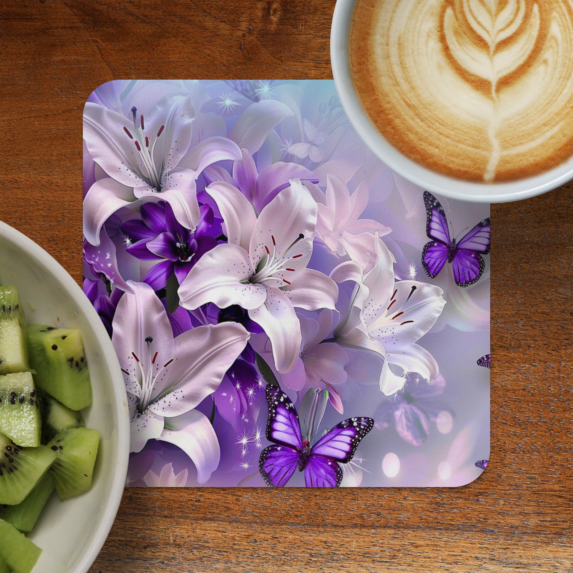 Lilies and purple butterflies on a patterned coaster next to kiwi fruit and coffee.