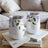 Two white tumblers with purple floral design and script text sit on books.