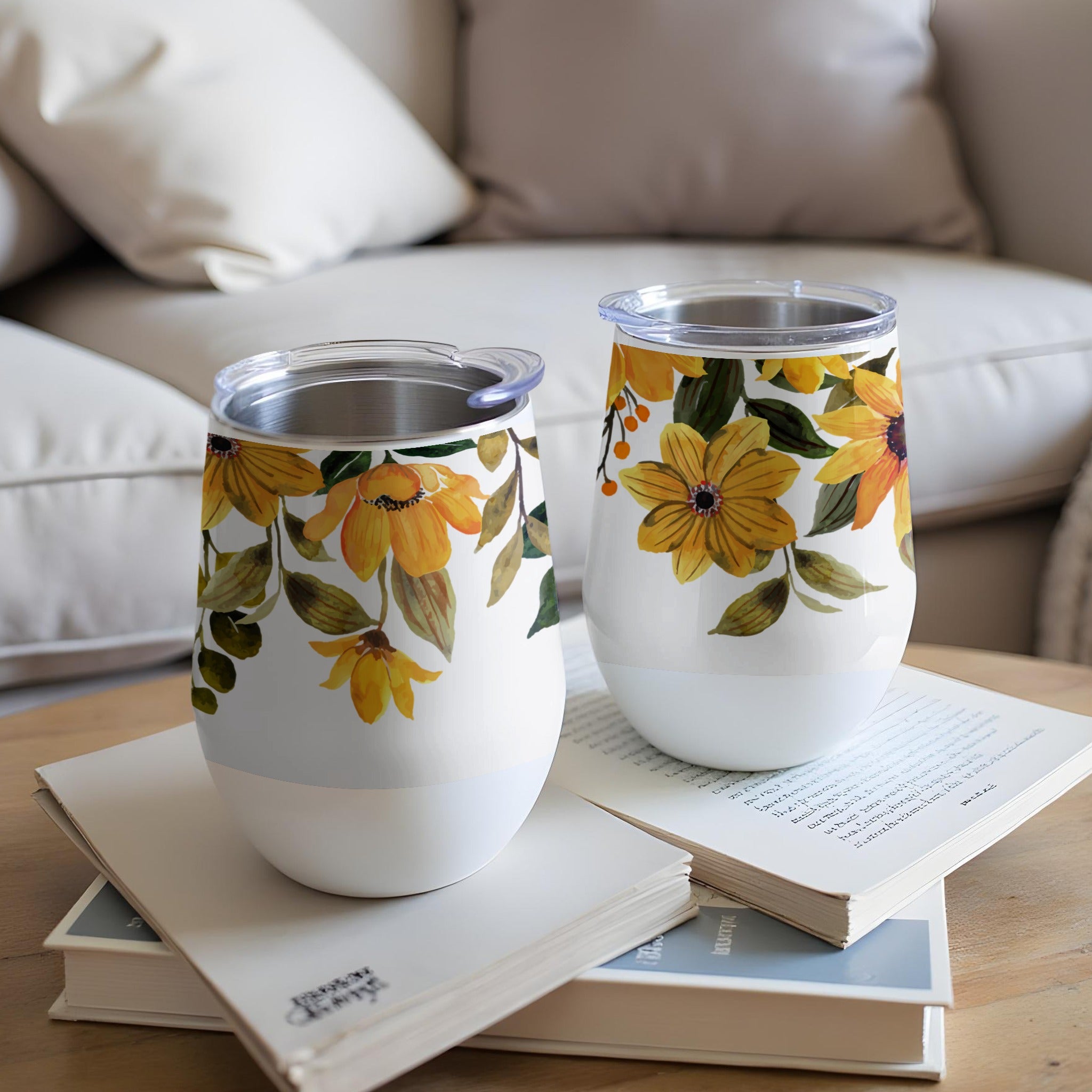 Two white tumblers with yellow floral designs on a stack of books.