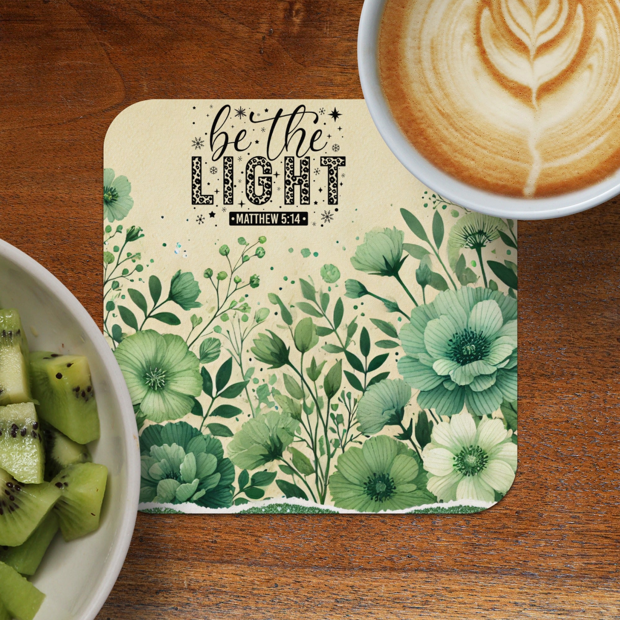 Coaster with "be the light" text and floral design, next to kiwi and coffee.