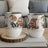 Two gnome couple mugs with hearts and floral designs, on a wooden coaster.