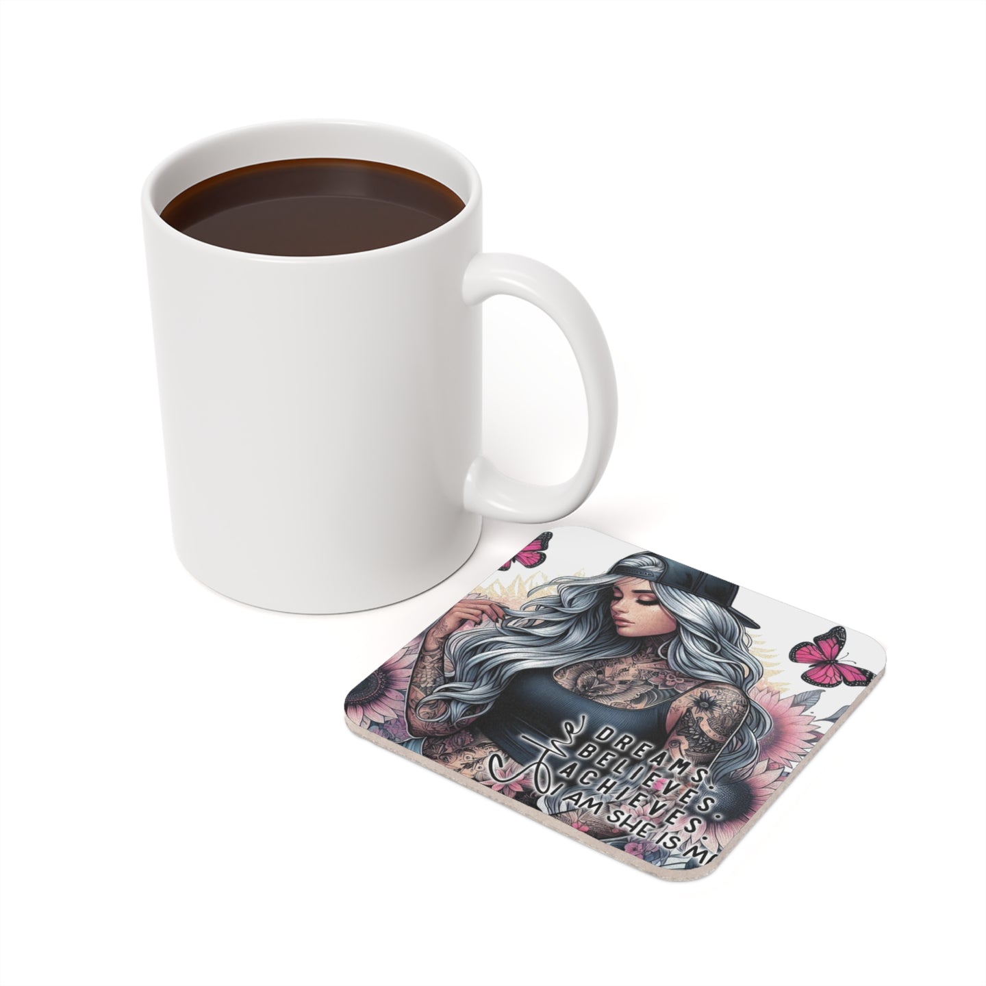 White mug of coffee next to a coaster with butterflies and text "DREAMS BELIEVE ACHIEVE AM SHE IS M".