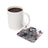 White mug of coffee next to a coaster with butterflies and text "DREAMS BELIEVE ACHIEVE AM SHE IS M".