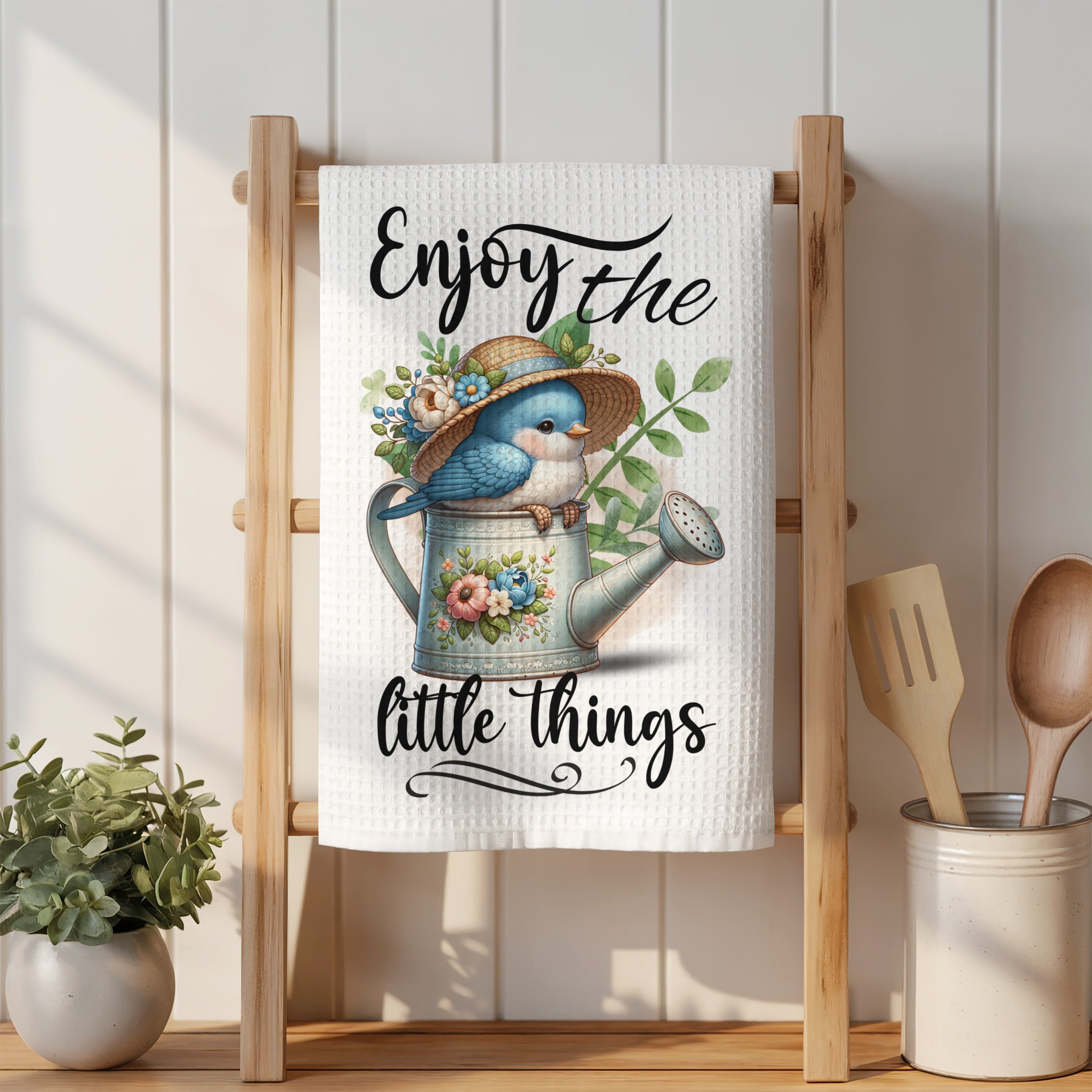 Blue bird wearing a straw hat sits in a watering can, "Enjoy the little things."