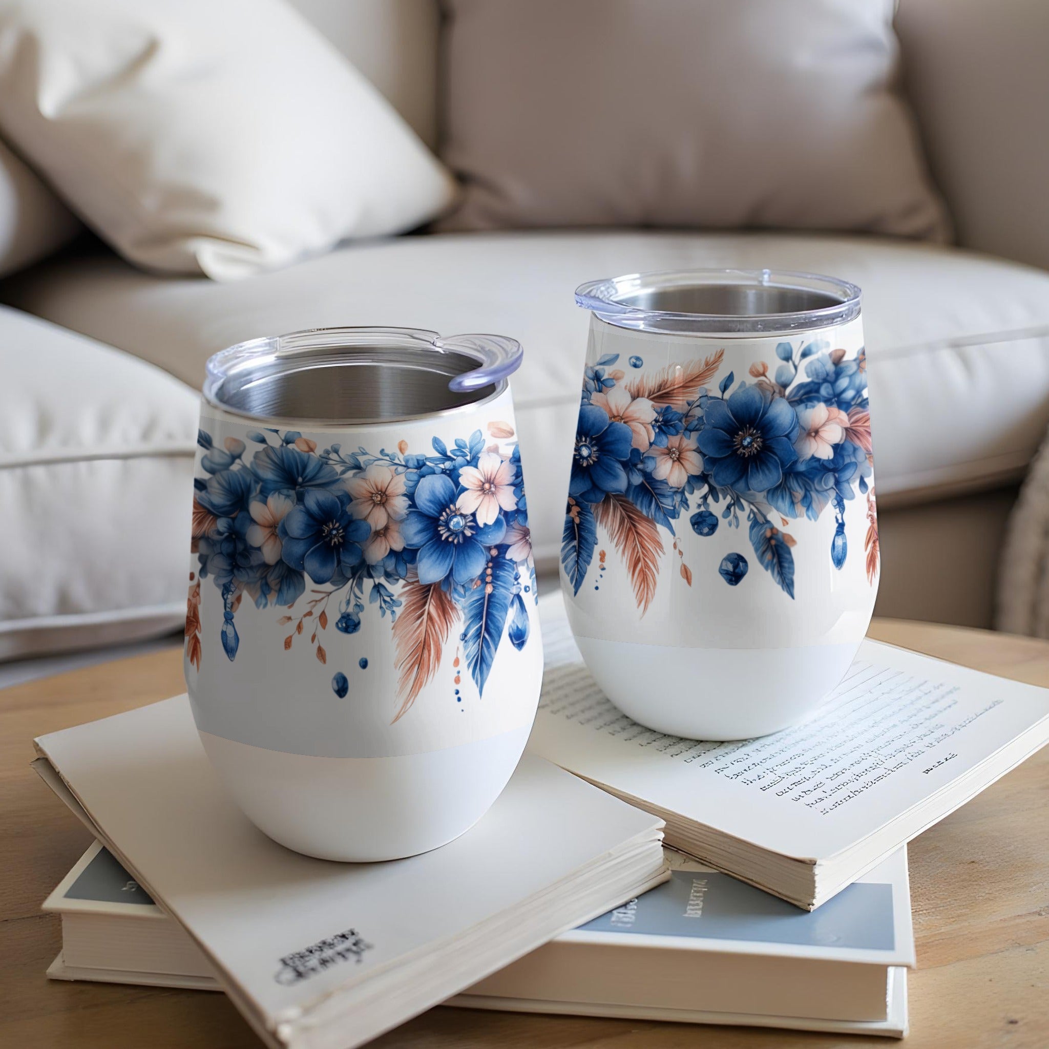 Two white stemless wine tumblers with blue floral and feather designs.