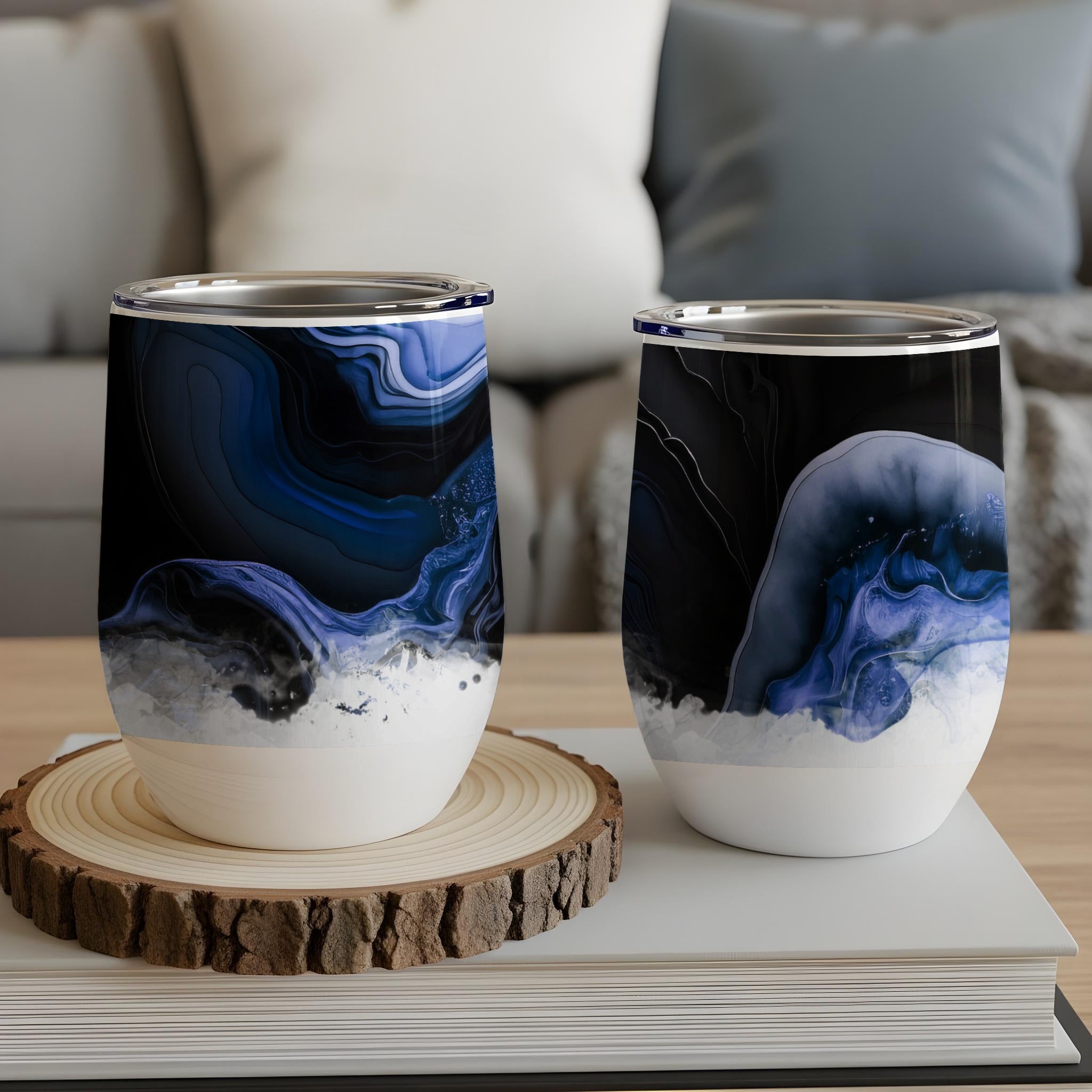 Two abstract art tumblers with blue and black marble design on a wooden coaster.