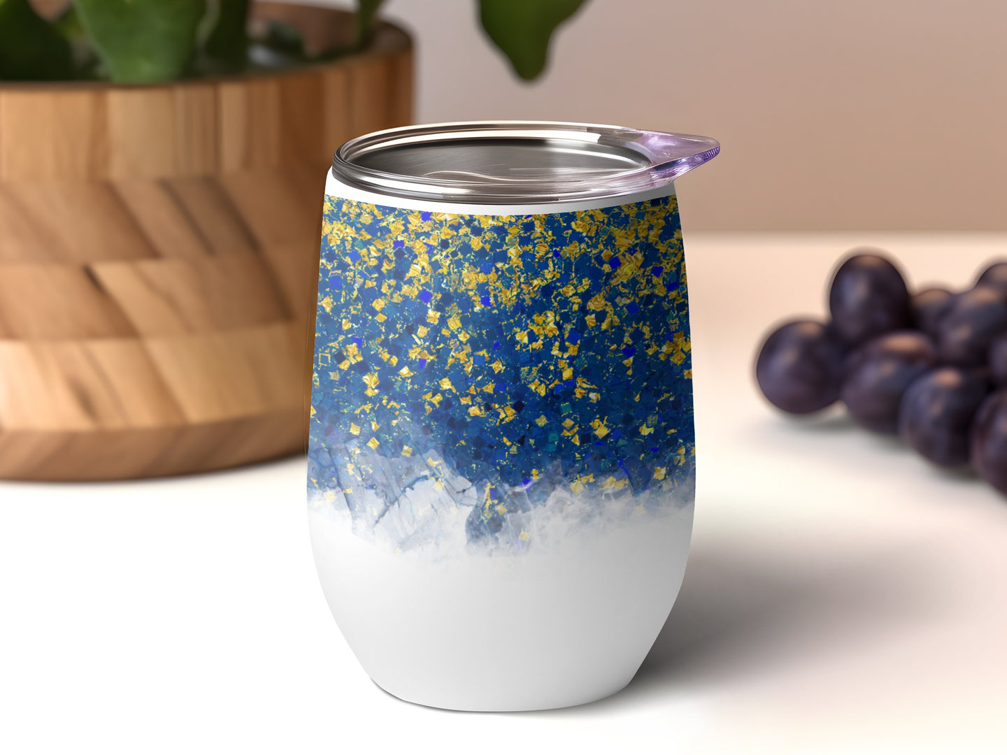 White tumbler with blue and gold glitter pattern, purple grapes nearby.