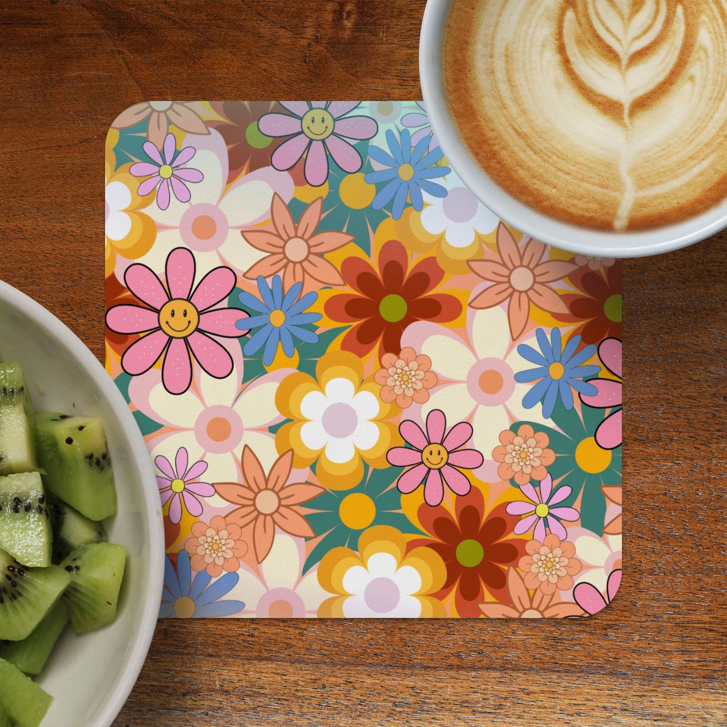 Retro floral coaster with smiling flowers beside kiwi and coffee.