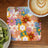 Retro floral coaster with smiling flowers beside kiwi and coffee.
