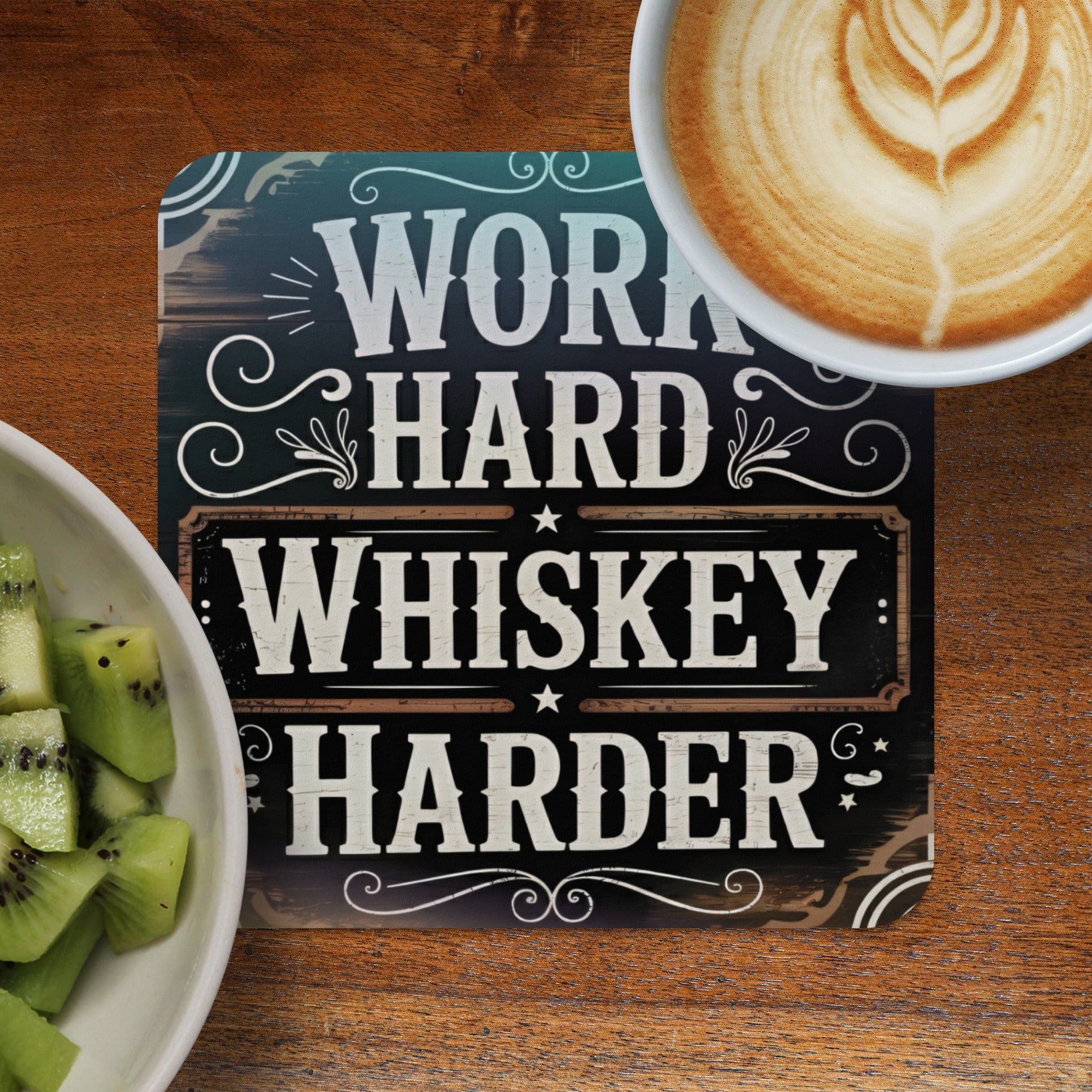 Coaster with "WORK HARD WHISKEY HARDER" text, next to coffee and kiwi.
