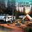 Camping scene with RV, tent, fire pit, and picnic table in forest at sunset.