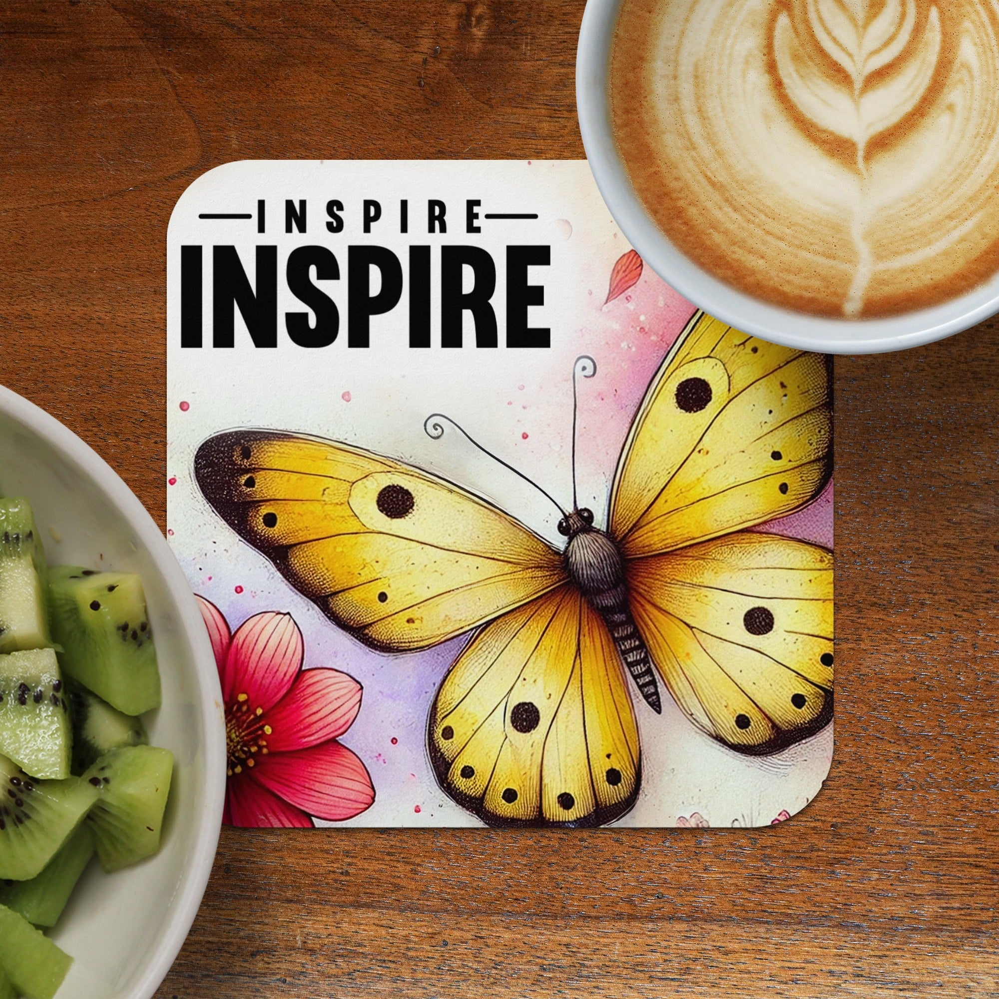 Yellow butterfly with black markings on inspirational coaster next to kiwi and coffee.