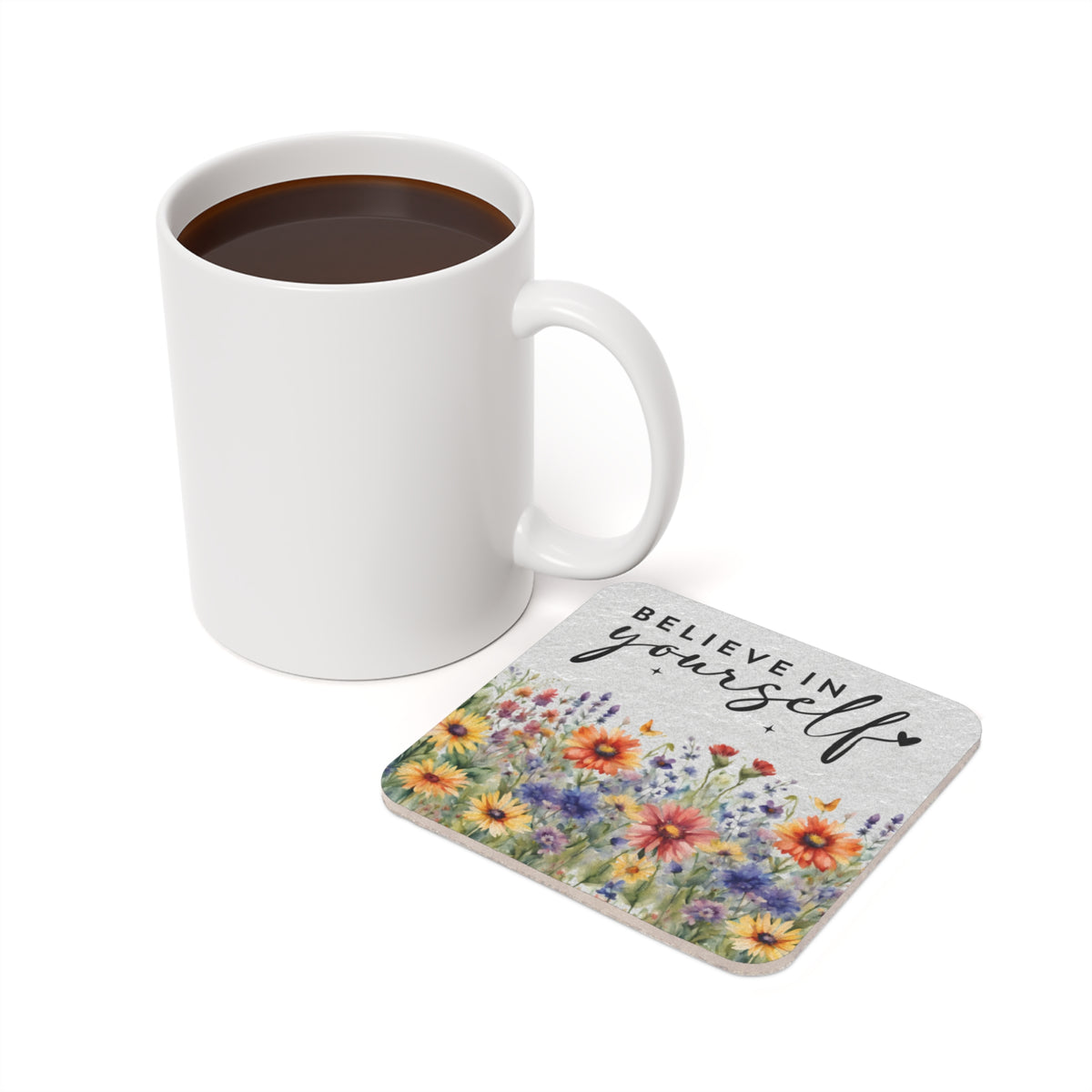 White mug with coffee next to floral coaster reading "BELIEVE IN yourself".