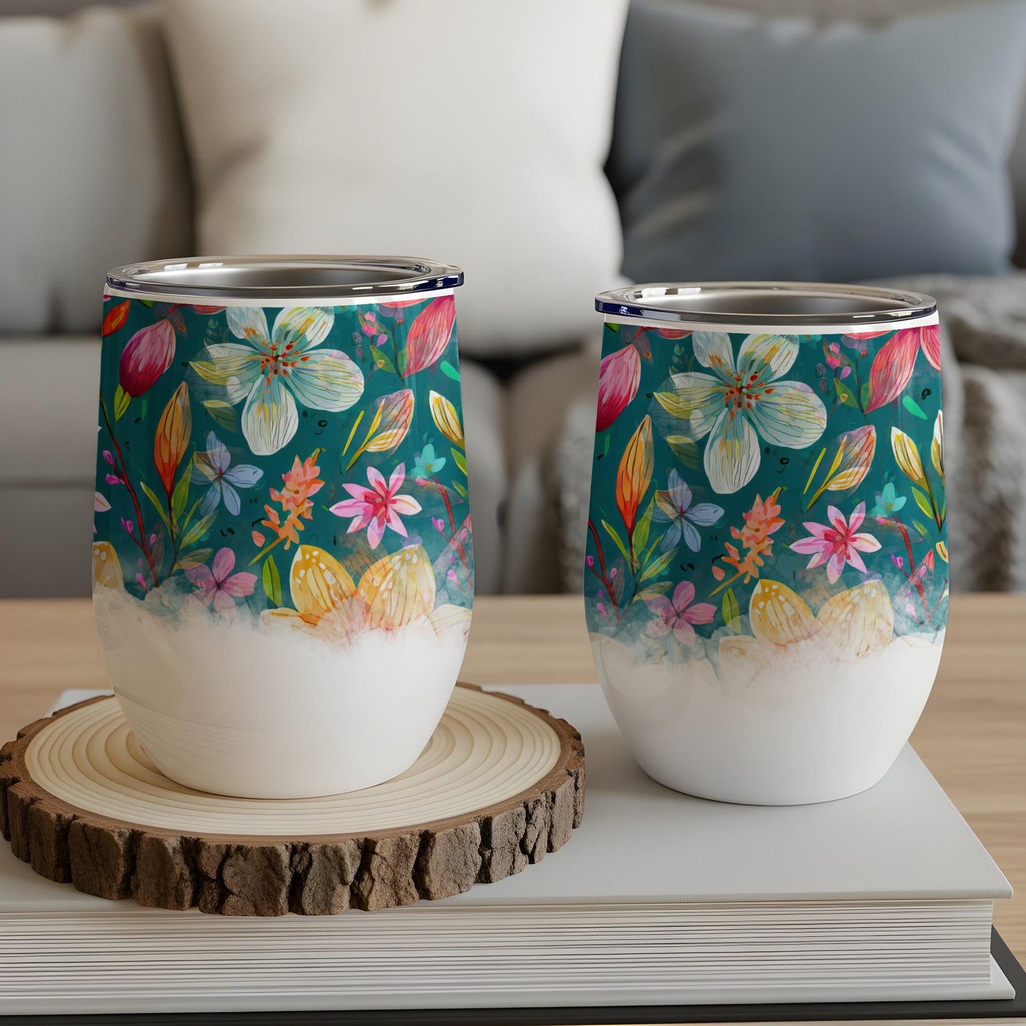 Two stemless wine tumblers with floral and egg designs on a wooden coaster.