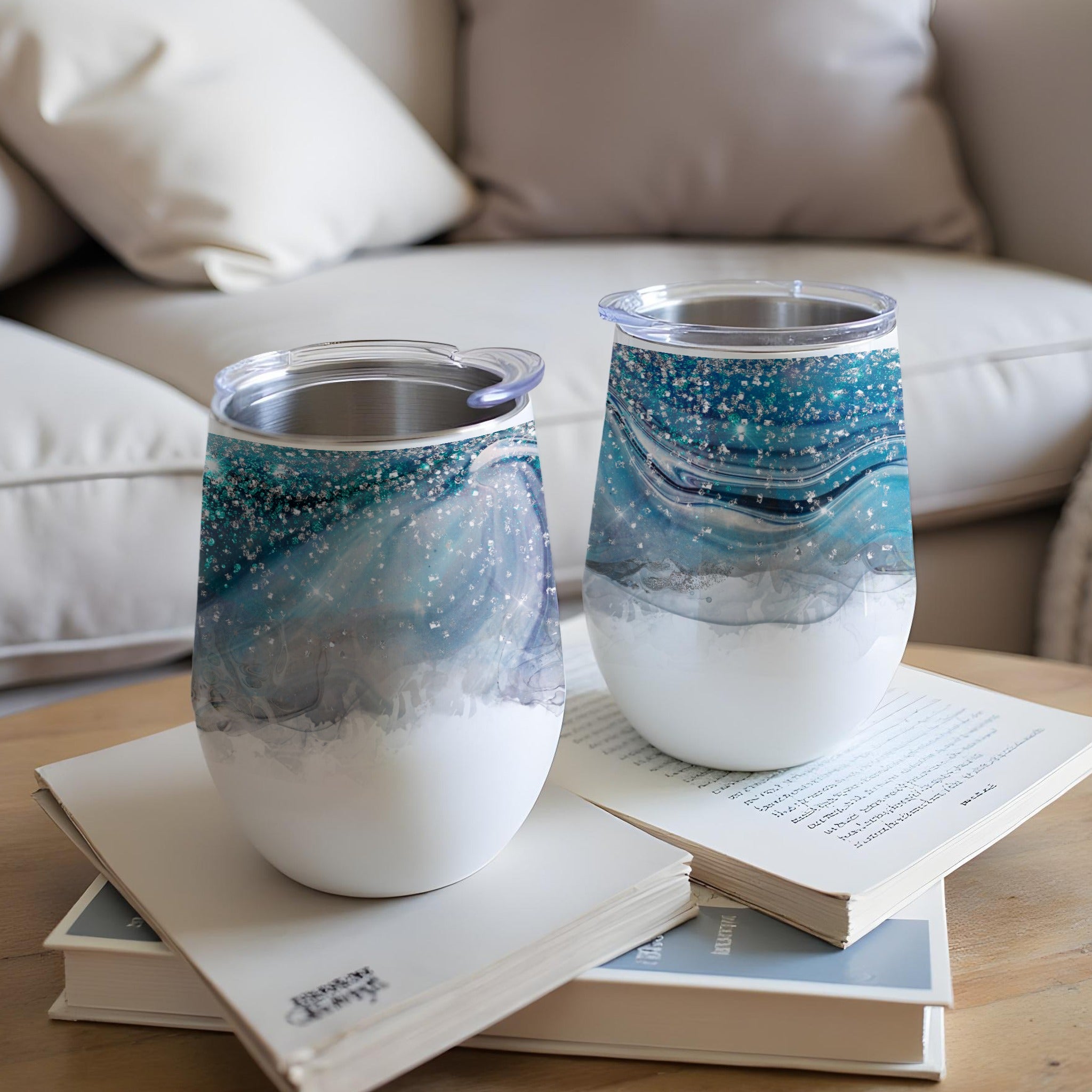 Two blue and white glittery tumblers on books with a blurred couch in the background.