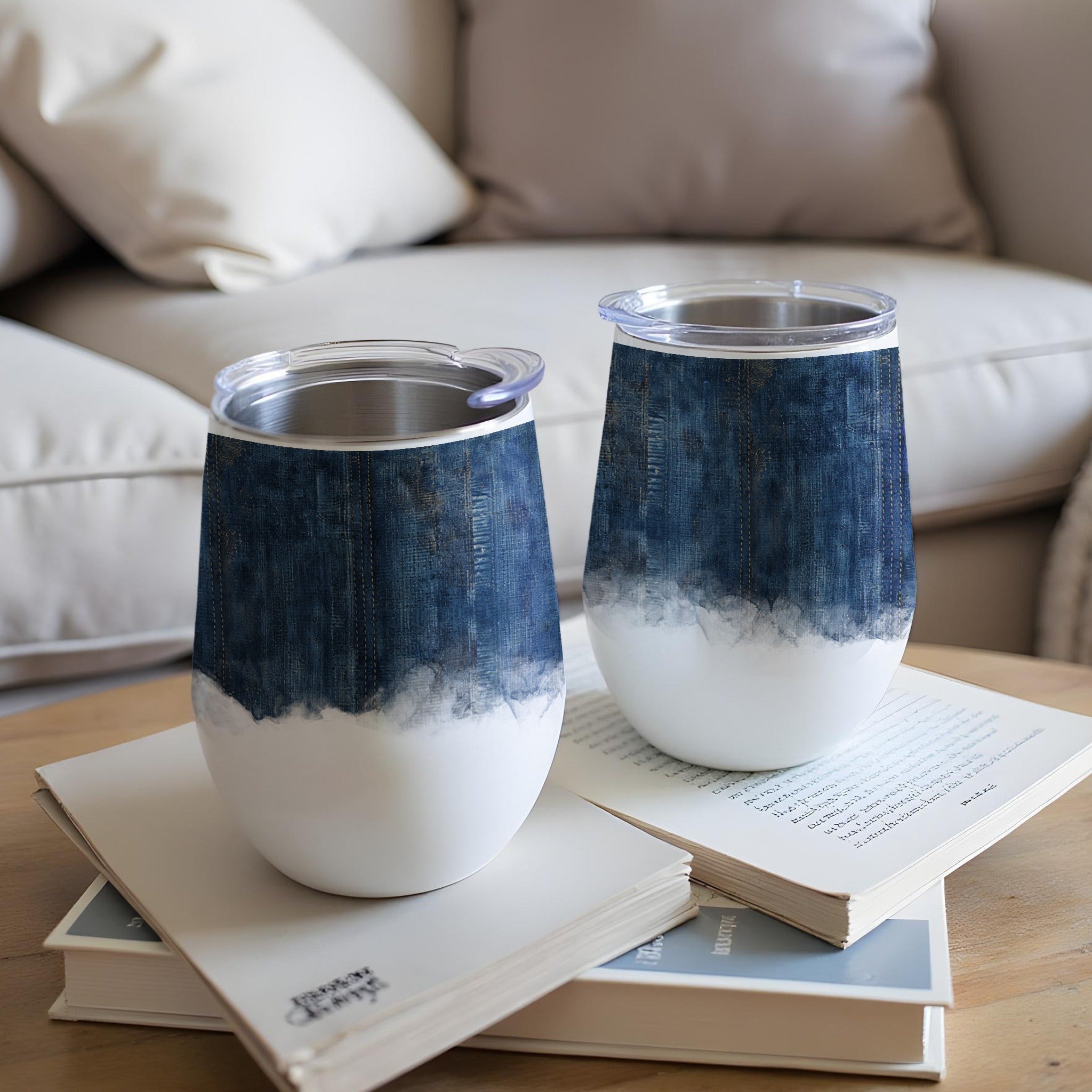 Two white tumblers with denim-inspired design and clear lids on books.