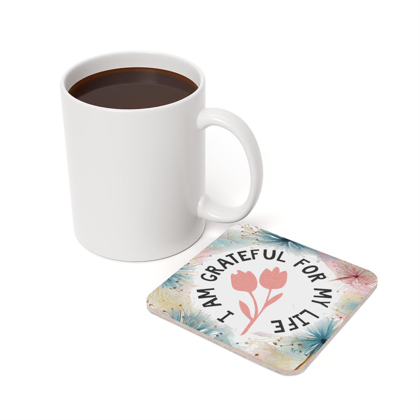 White mug of coffee next to a square coaster with flowers and text "I AM GRATEFUL FOR MY LIFE".