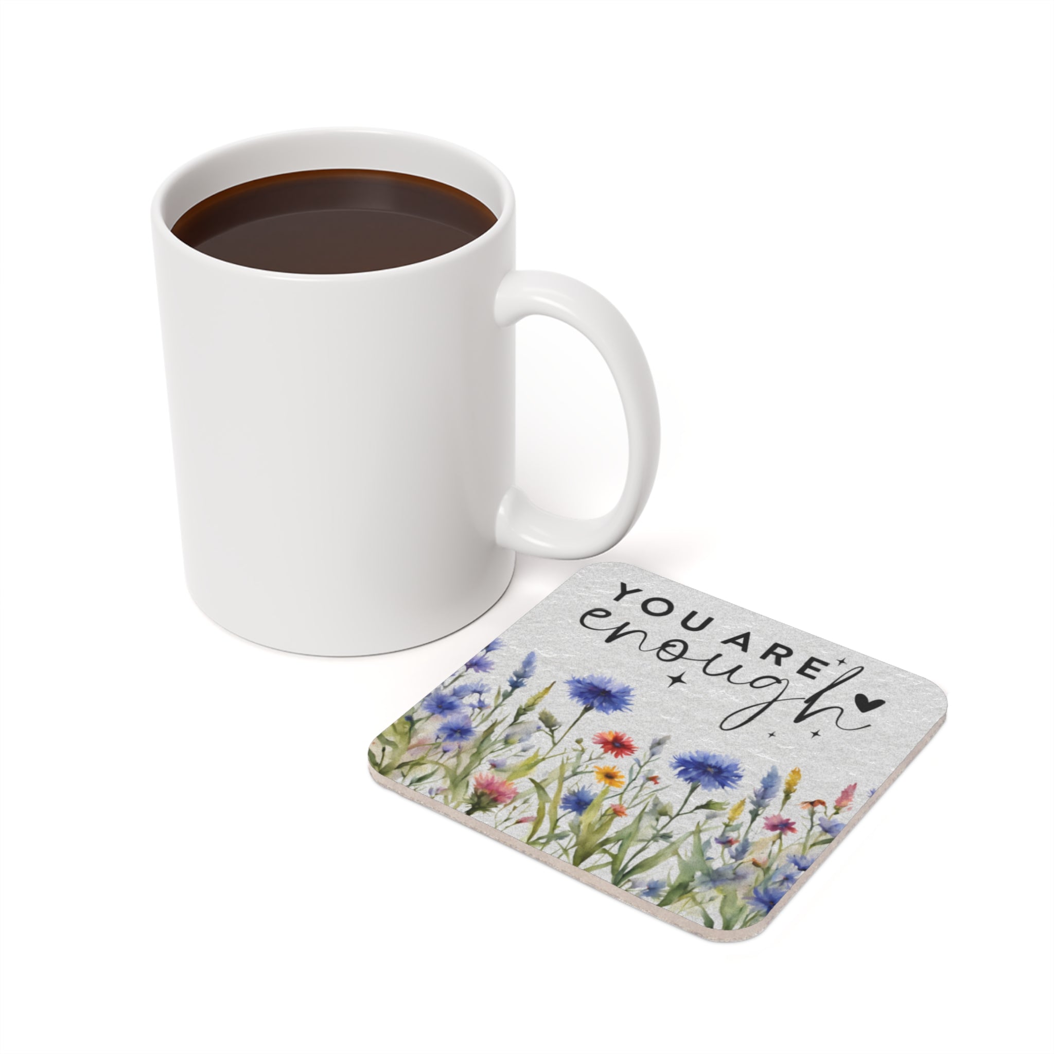 White mug of coffee next to a coaster with watercolor flowers and "you are enough" text.