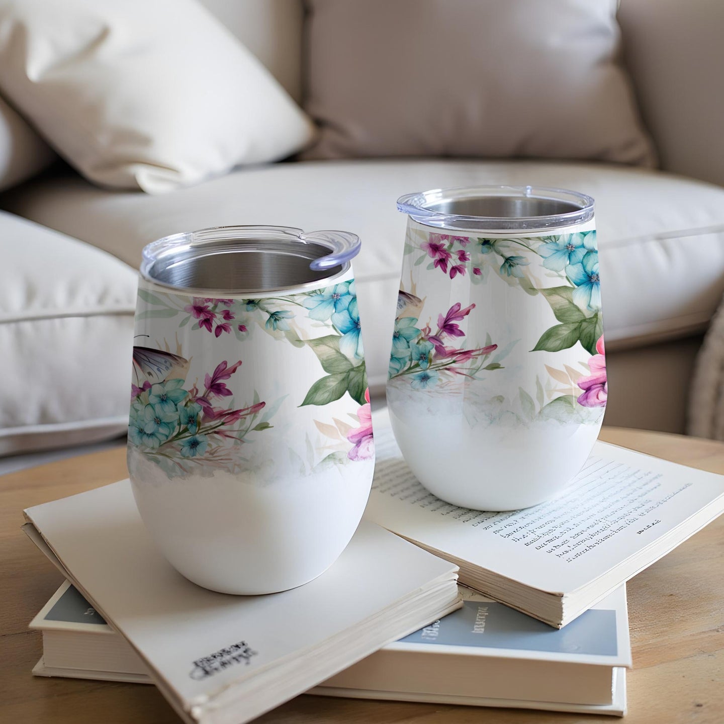Two white tumblers with floral designs sit on a stack of books.