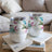 Two white tumblers with floral designs sit on a stack of books.