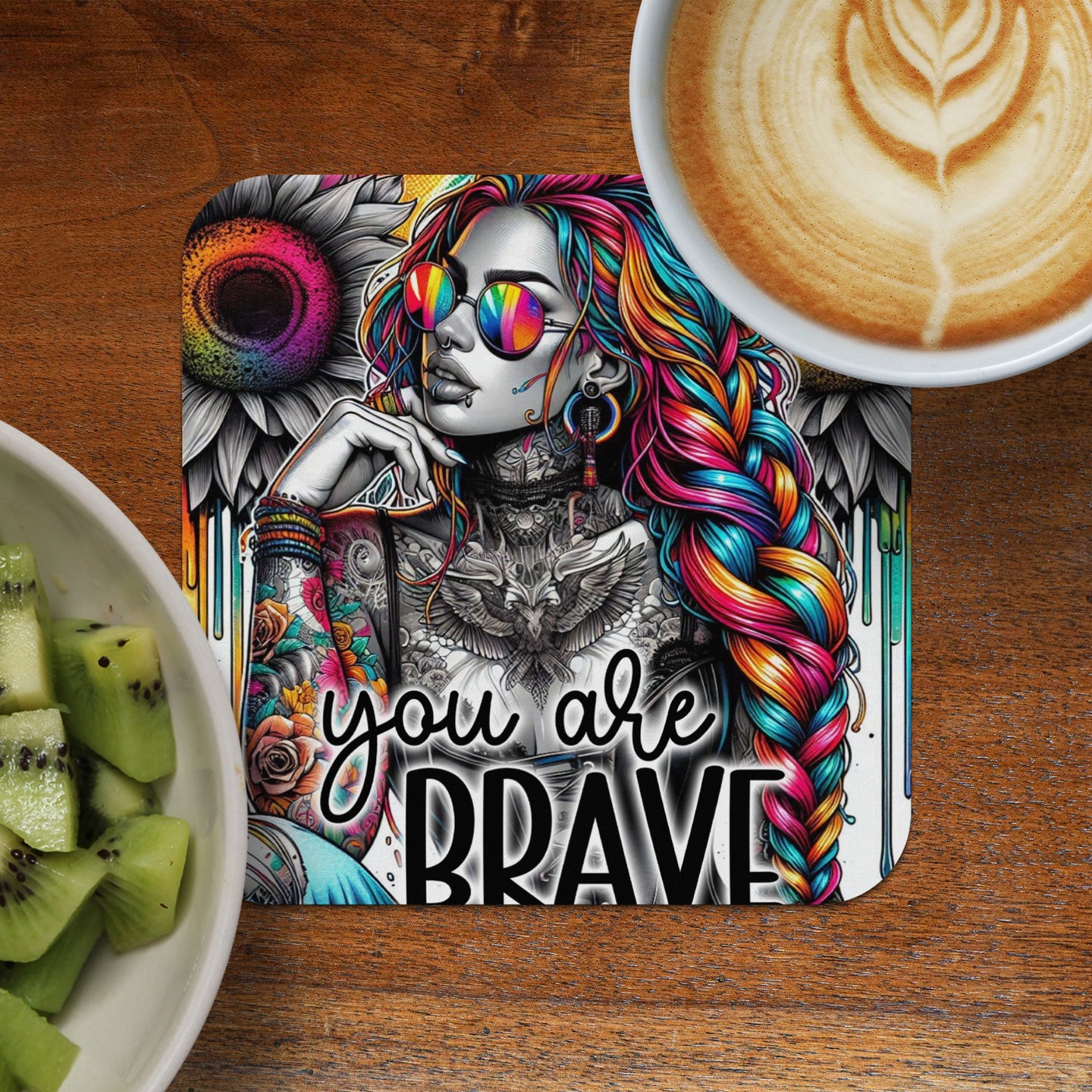 Woman with rainbow hair, sunglasses, and "you are brave" text on a coaster.