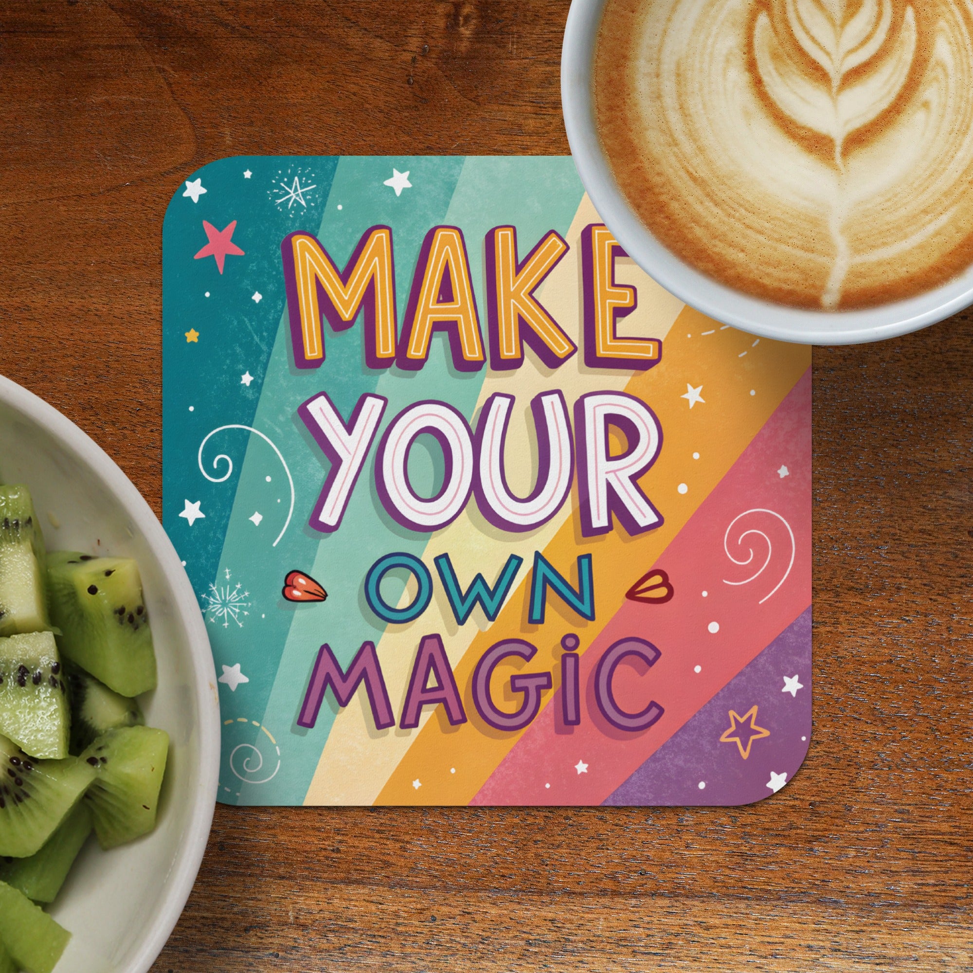 Colorful coaster with "Make Your Own Magic" text next to coffee and kiwi.