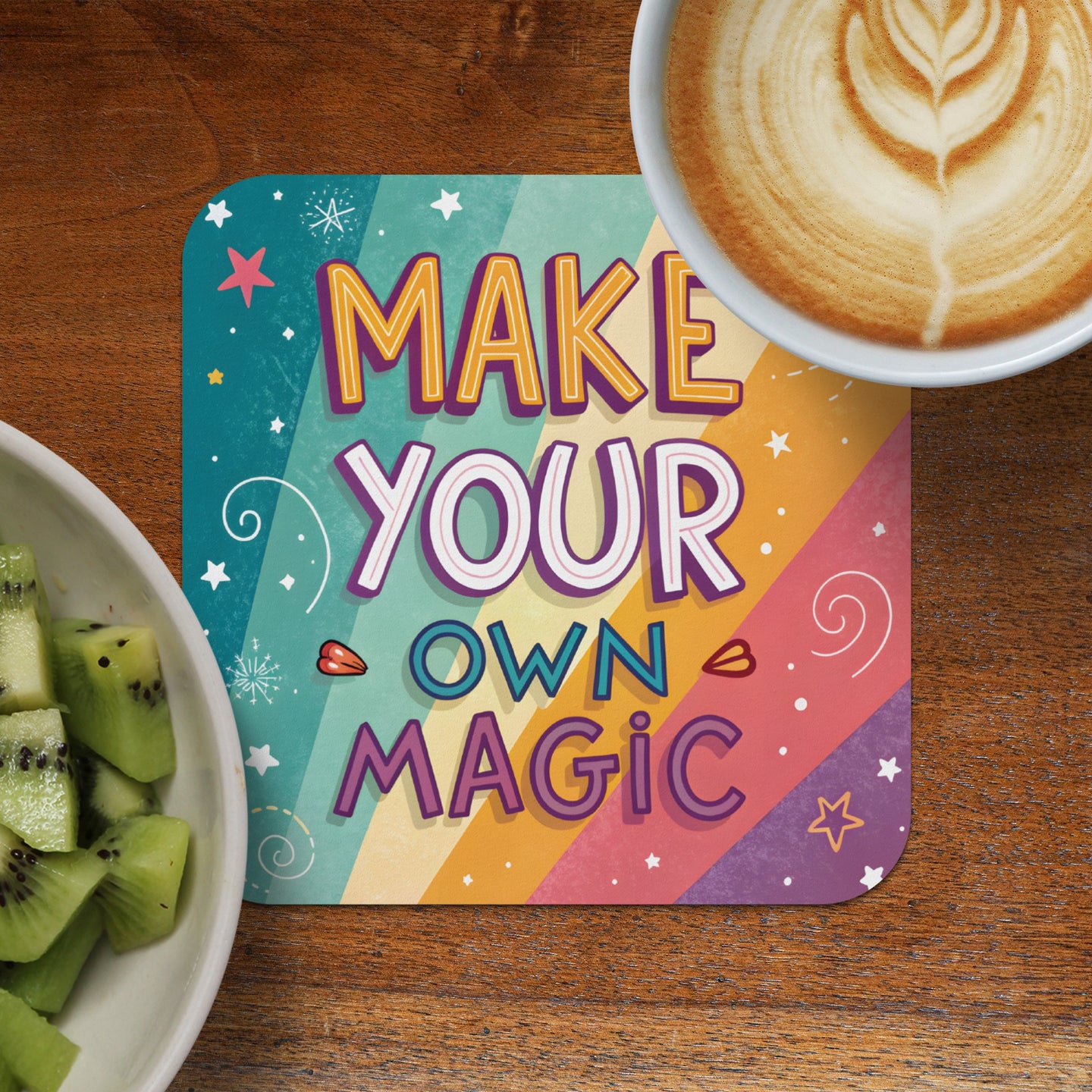 Colorful coaster with "Make Your Own Magic" text next to coffee and kiwi.