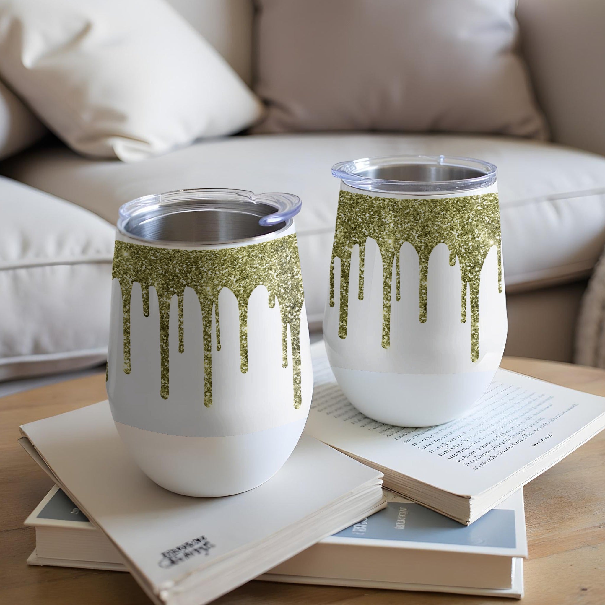 Two white tumblers with green glitter drips sit on a stack of books.