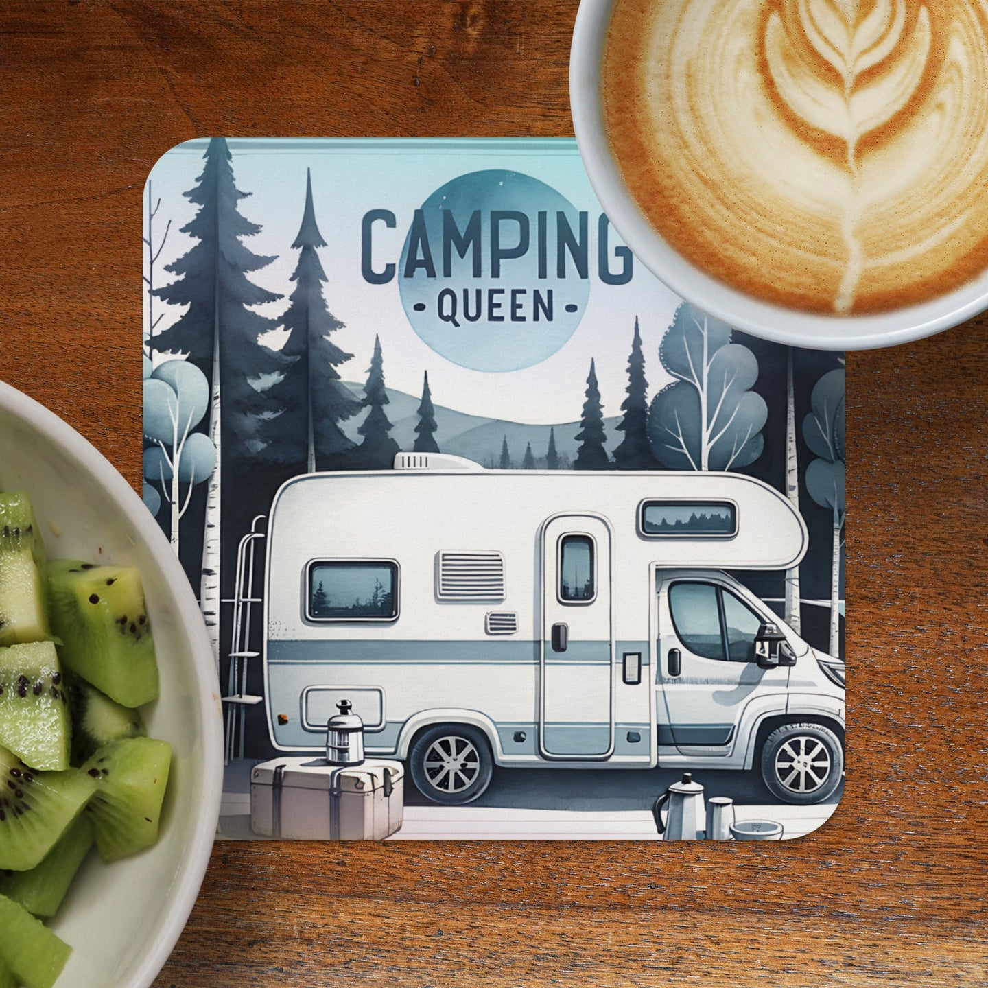 RV with "Camping Queen" text and forest scene on a coaster, next to kiwi slices and coffee.