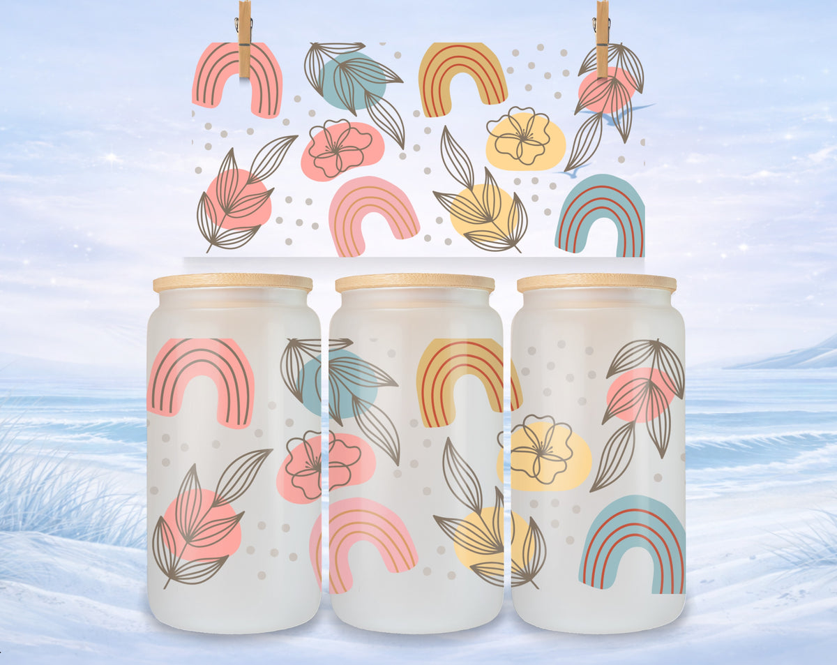 Glass can cups with pastel rainbow and leaf designs on a snowy background.