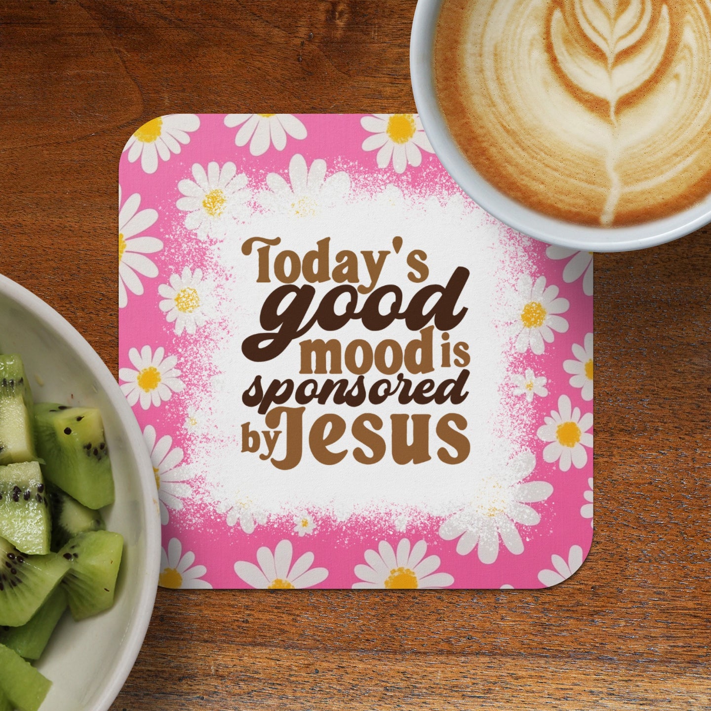 Coaster with daisies and text "Today's good mood sponsored by Jesus" next to kiwi and coffee.
