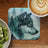 Wolf head illustration on a forest-themed coaster beside kiwi and coffee.