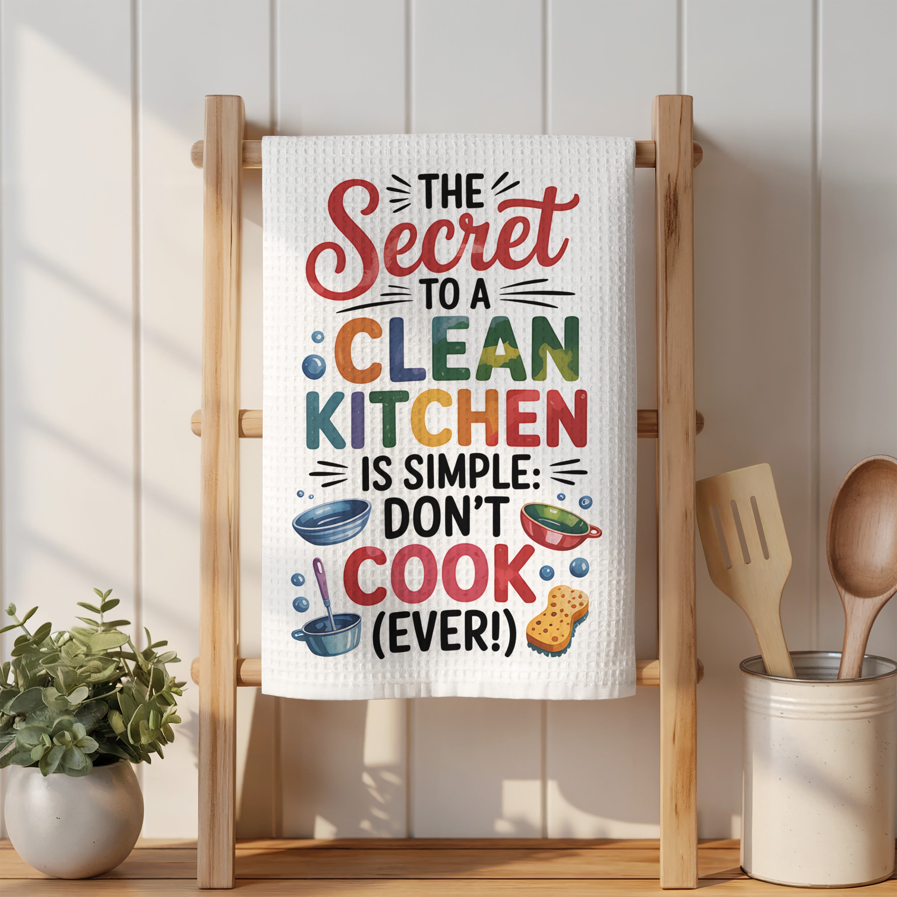 White kitchen towel with colorful "The Secret to a Clean Kitchen is Simple: Don't Cook (Ever!)" text.