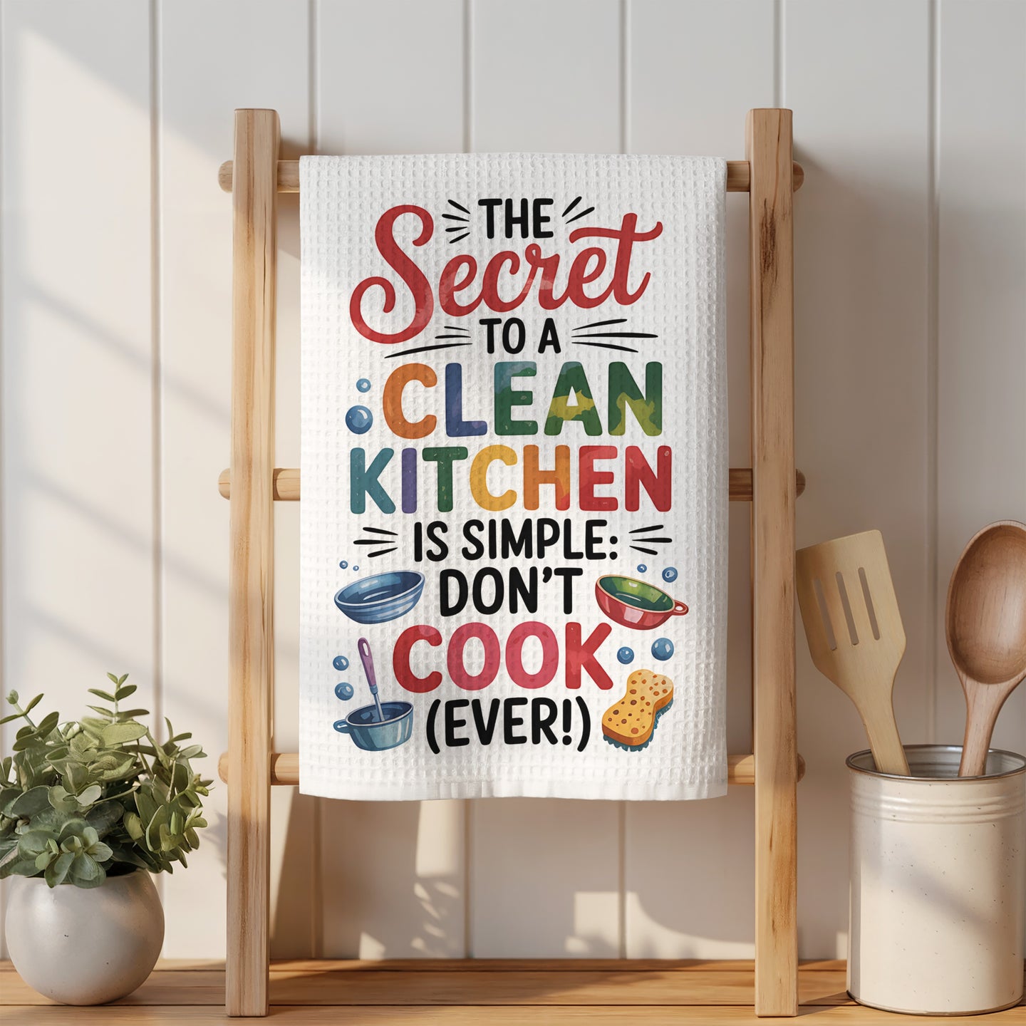 White kitchen towel with colorful "The Secret to a Clean Kitchen is Simple: Don't Cook (Ever!)" text.