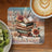 Stack of books with flowers and feathers, latte, and kiwi slices.