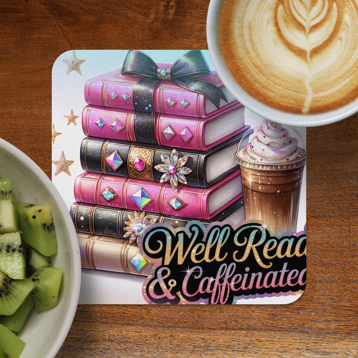Stack of decorative pink books with bow and jewels next to coffee and kiwi slices.