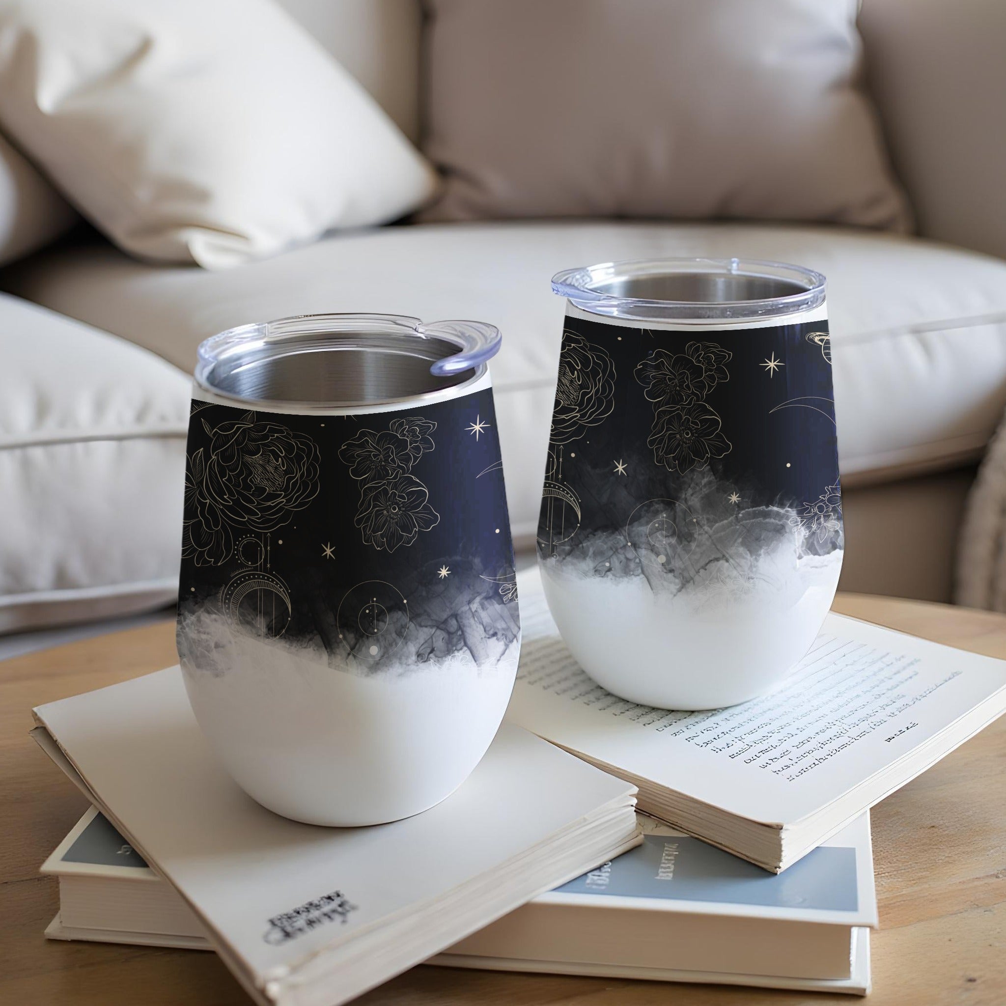 Two white tumblers with celestial designs sit on books.
