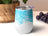 White tumbler with blue abstract watercolor design and purple grapes in background.