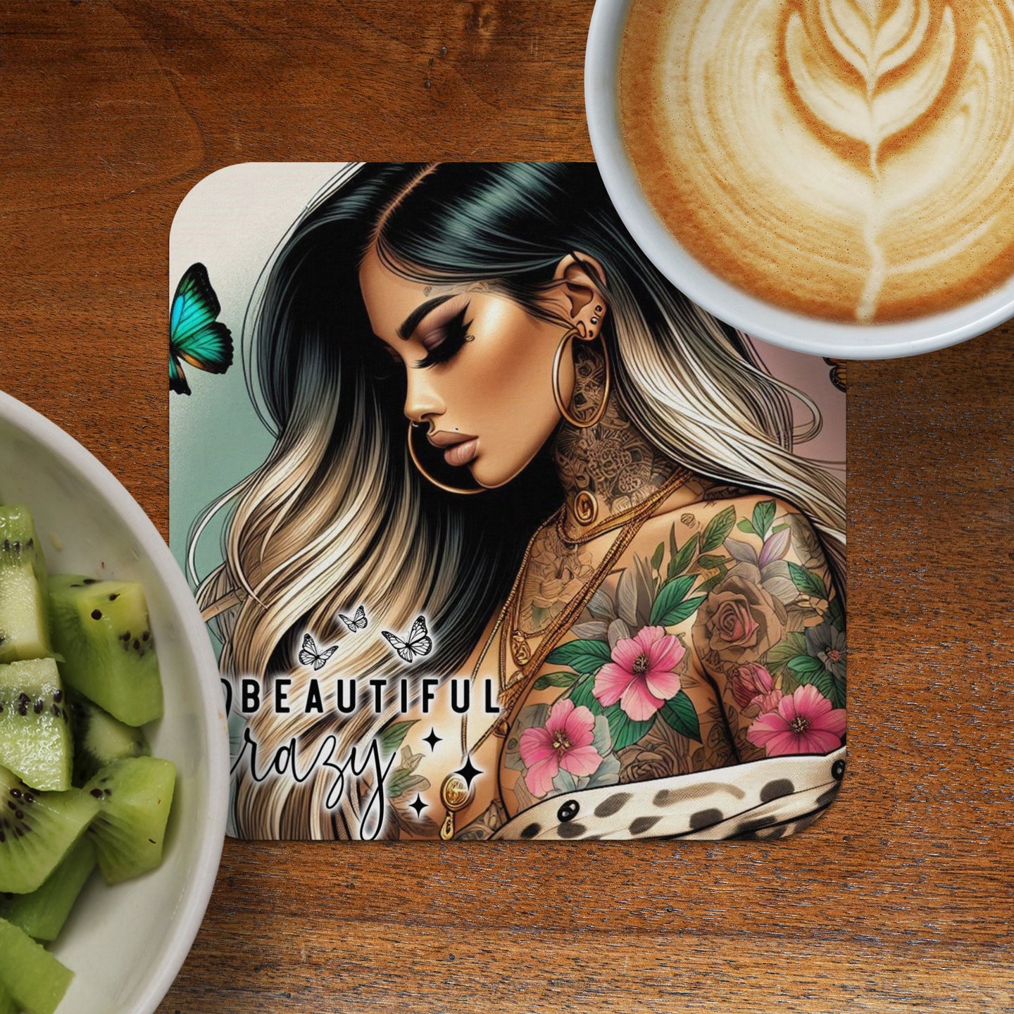 Woman with colorful tattoos and butterfly art on coaster, next to coffee and kiwi.