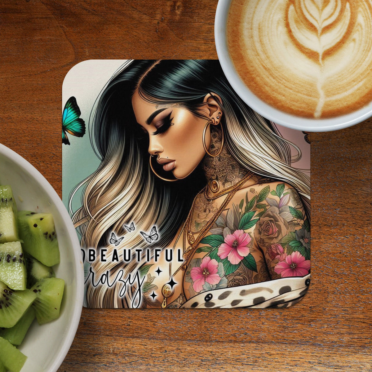 Woman with colorful tattoos and butterfly art on coaster, next to coffee and kiwi.