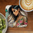Woman with colorful tattoos and butterfly art on coaster, next to coffee and kiwi.