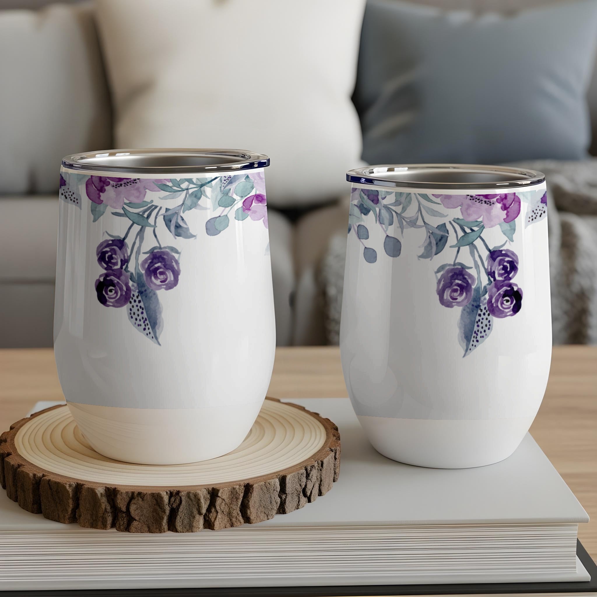 Two white tumblers with purple floral design, resting on a wood slice and books.